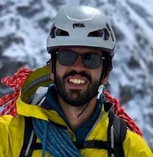 Un hombre con una chaqueta amarilla sonríe frente a una montaña nevada, luciendo la mejor protección solar facial.