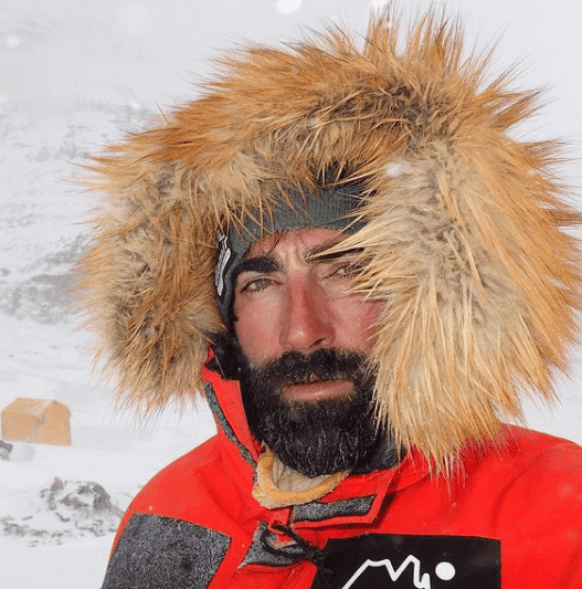 mejor-proteccion-solar-facial Un hombre barbudo con una chaqueta roja parado en la nieve.