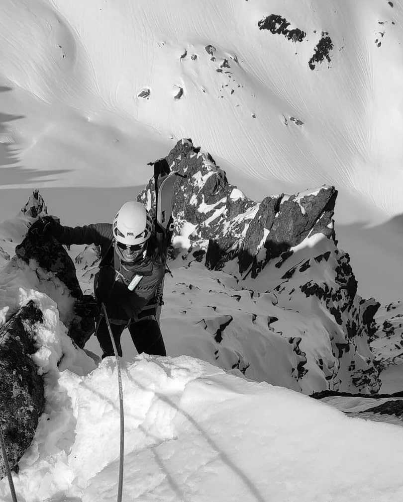 Una fotografía en blanco y negro de una persona escalando una montaña nevada. Lleva crema solar para escalada colgada del pecho.