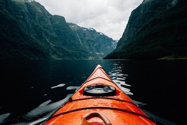 Un kayak en un lago con las montañas de fondo, protegido con crema solar y utilizando el mejor labial y facial.