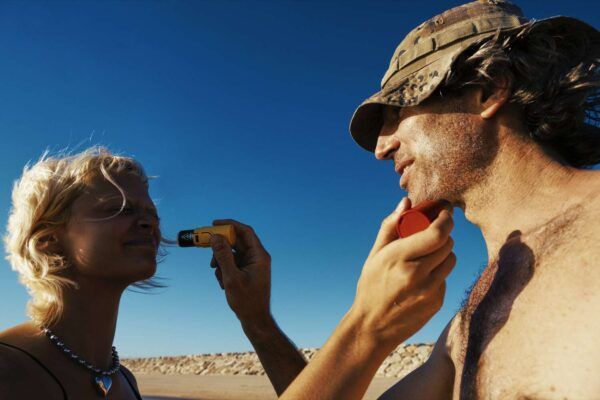 mejor-proteccion-solar-facial Una persona aplica crema solar resistente al agua en el rostro de otra persona mientras está de pie al aire libre bajo un cielo azul claro.